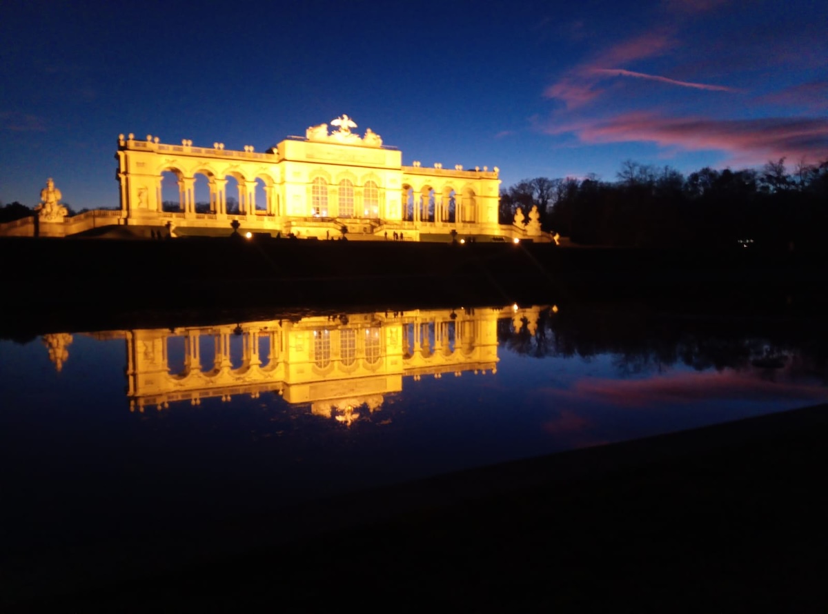 Beleuchtete Gloriette bei Sonnenuntergang mit Spiegelung im Wasser.